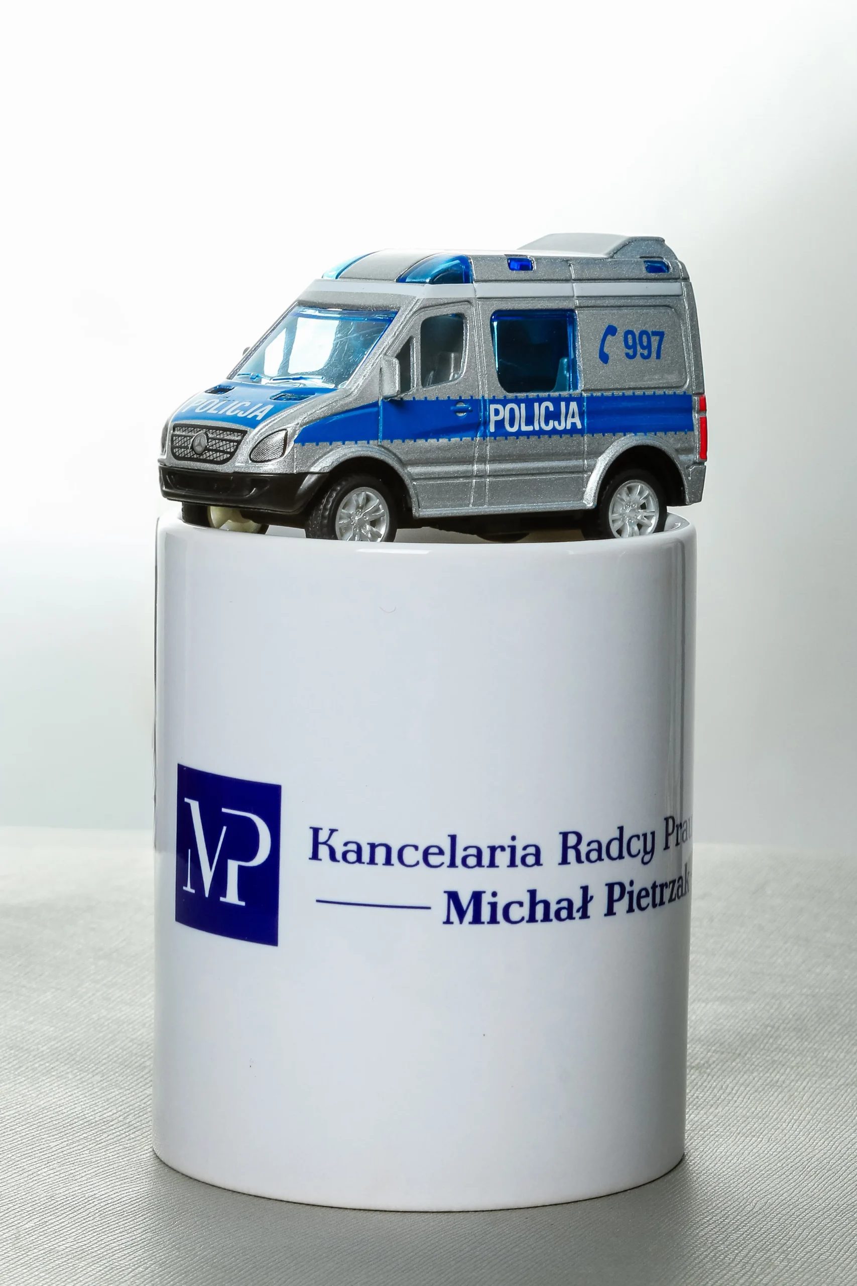 zdjęcie kubka Kancelarii Rady Prawnego Michała Pietrzaka, z radiowozem policyjnym stojącym na kubku